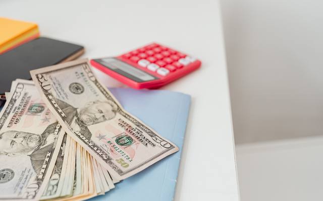 Fanned US banknotes beside a calculator on a white desk