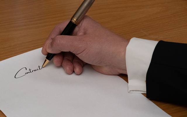 A hand signing a printed contract at a wooden desk
