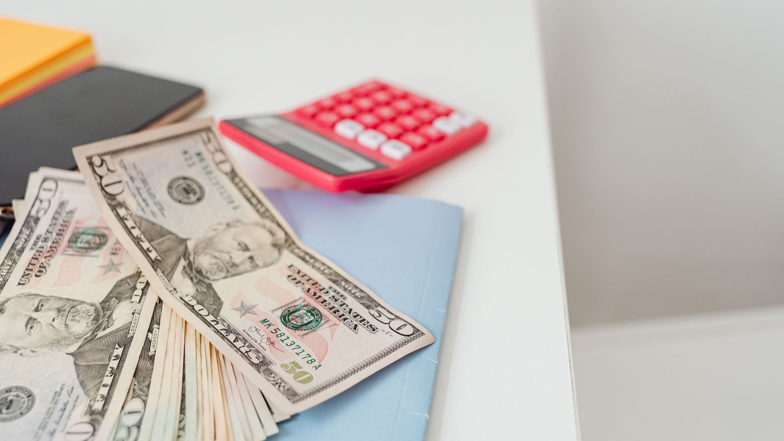 Fanned US banknotes beside a calculator on a white desk