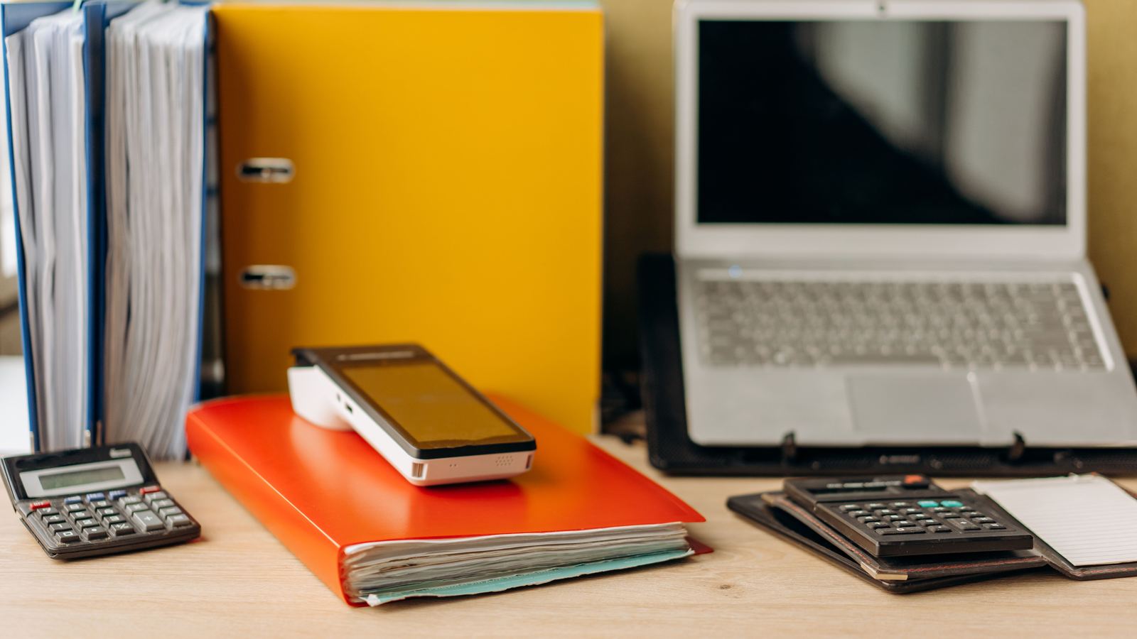 Desk in daylight with document folders, a calculator and an open laptop