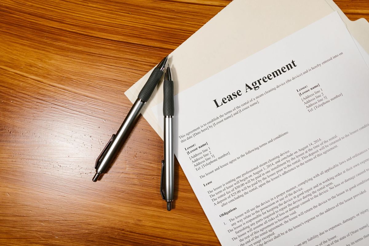 Printed lease agreement with two pens lying on a wooden desk