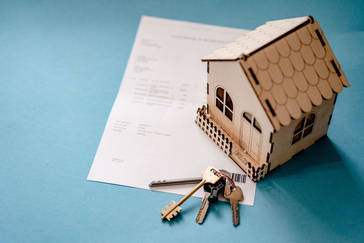 Wooden model house and a set of keys resting on a printed rental document