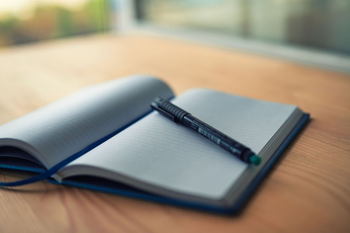 Open ruled notebook and pen on a wooden desk beside a window