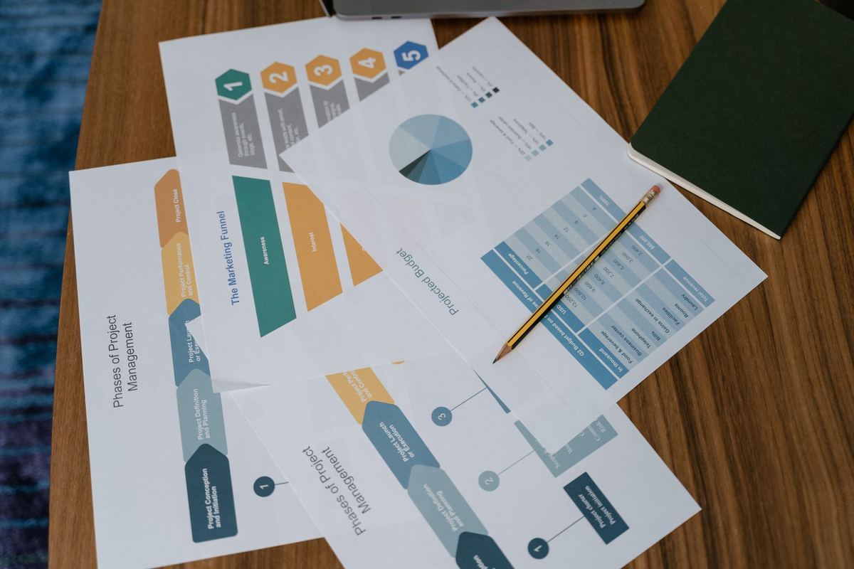Printed planning sheets and charts spread across a wooden table with a pencil