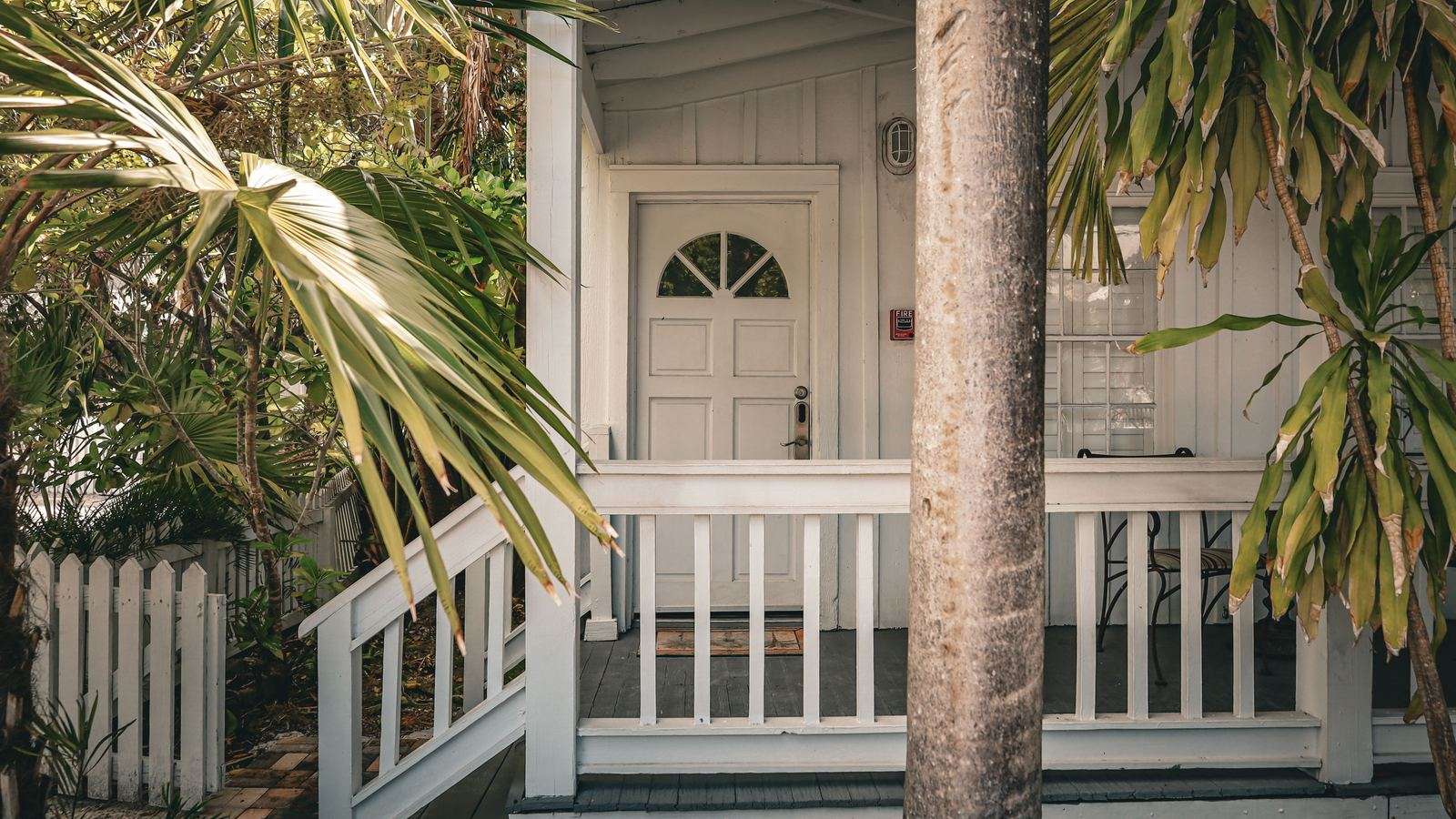 Covered wooden porch of a small rental house behind a white picket fence